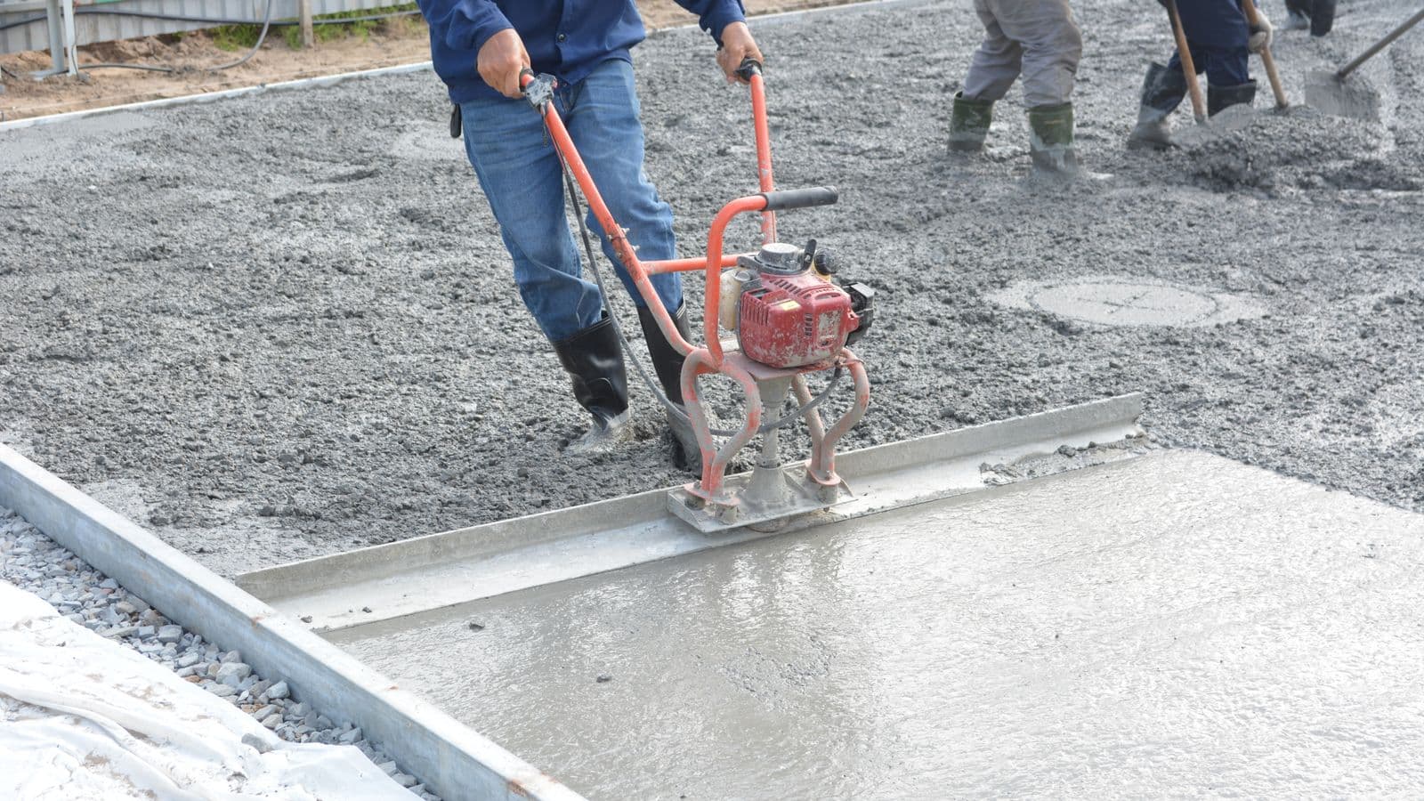 A worker power-troweling the surface of a freshly poured concrete slab on an outdoor site.